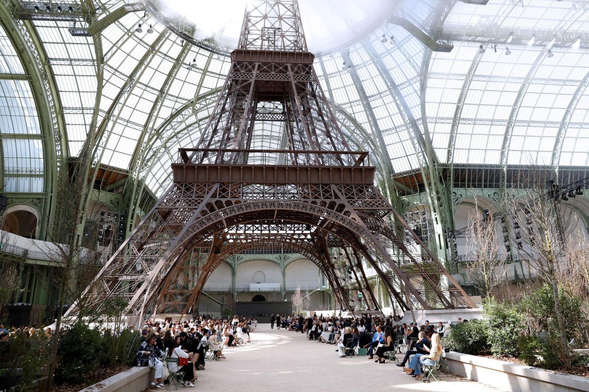 Desfile de moda no Grand Palais em Paris com estrutura inspirada na Torre Eiffel durante semana de moda internacional