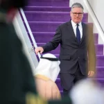 Keir Starmer desce escadas em chegada oficial durante contexto de crise internacional com o Irão