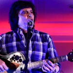 Luís Represas atua em palco durante um concerto, numa imagem que homenageia a voz histórica dos Trovante e da música portuguesa.